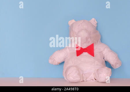 Teddybär mit roter Schleife binden in weißes Papier für ein Geschenk auf blauem Hintergrund gewickelt Stockfoto