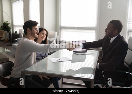 Glückliches junges Paar Hände schütteln mit afrikanischen amerikanischen Finanzberater. Stockfoto