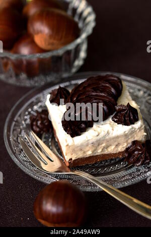 Stück Sweet Chestnut Creme Kuchen serviert auf transparentem Glas Dessertteller mit Kastanien im Hintergrund. Herbst saisonal keto Dessert Stockfoto