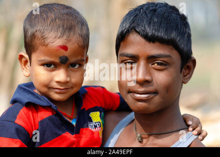 CHANDANPUR, Indien, 14. JANUAR 2019: Portrait von indischer Junge seinen kleinen Bruder Holding in der Straße Stockfoto