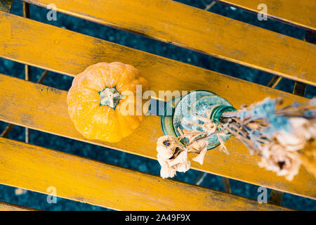 Kürbis und welken Strauß Blumen in einer Flasche auf einem gelben Holztisch. Ausgewählte konzentrieren. Stockfoto