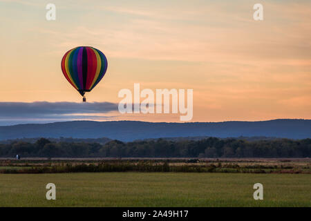 Rainbow Heißluftballon schwebt über auf dem Feld bei Sonnenaufgang Stockfoto