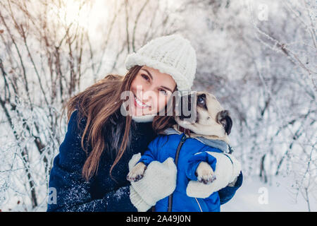 Pug dog walking im Freien. Frau umarmen Pet in Winter Park. Welpen tragen Winter mit Schnee bedeckt. Stockfoto