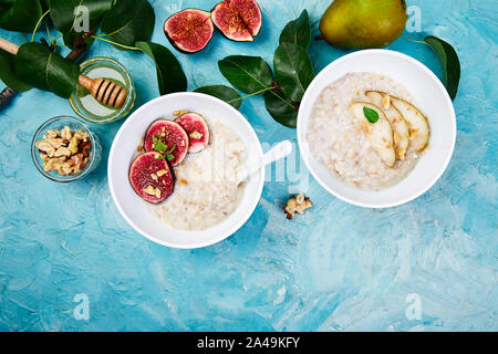 Gesundes Frühstück. Eine Schüsseln mit Porridge mit Birnen und Walnüssen und Haferbrei mit Feigen auf blauem Hintergrund. Zwei Schüsseln. Flach. Kopieren Sie Platz. Top Stockfoto