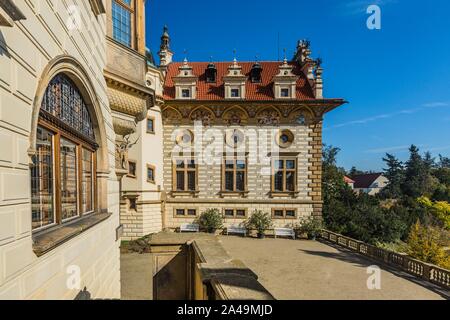 Prag, tschechische Republik - 7. Oktober 2019: Schloss mit beige Fassade und rotem Dach stehend auf einen Innenhof mit weißen Bänke an einem sonnigen Herbsttag. Stockfoto