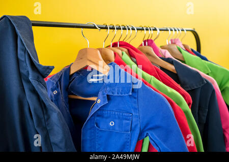 Multi-farbigen Kinder Berufsbekleidung für kreative Arbeit hängt an den Kleiderbügeln, vor dem Hintergrund der hellen gelben Wand, in einem Kids Club. Close-up. Stockfoto