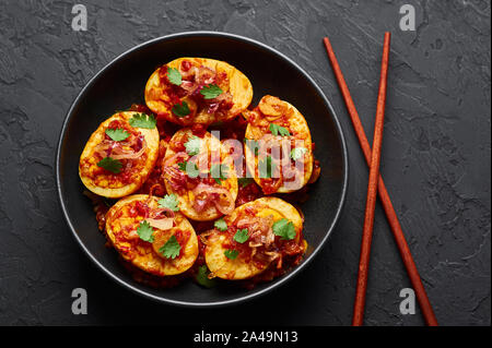 Goldene Ei Curry in schwarz Schüssel am dunklen Schiefer Hintergrund. Die burmesische Ei Curry ist beliebt Myanmar Küche Teller mit Ente oder Huhn Eier, Tomaten, Ingwer Stockfoto