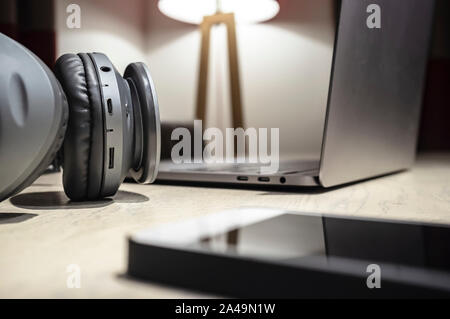 Kopfhörer, ein Laptop und ein Handy liegen auf einem hölzernen Tisch in einer gemütlichen Atmosphäre. Musikalische Konzept. Close-up. Stockfoto