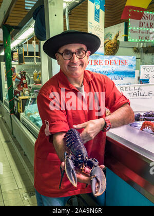 Blaue Hummer FRANKREICH BRETONISCHE FISCHHÄNDLER CLEUNES FISCH MARKTSTAND CONCARNEAU FRANKREICH BRETAGNE Concarneau täglich innen Französisch Fisch Markthalle und Charakter Fischhändler, im bretonischen Stil Outfit stolz seinen lokalen live Blue Lobster Anzeigen zum Verkauf bretagne finistere Frankreich Stockfoto