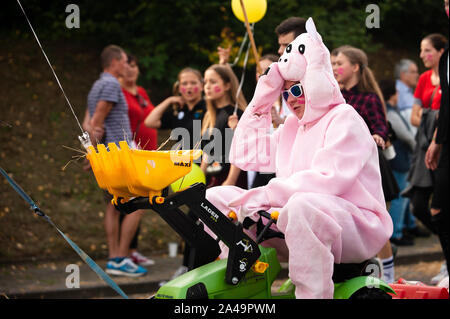 Deutschland, Niederstetten, Baden Württemberg. September 2019. Traditionelle herbstliche Ernte Fest. Junger Mann in pig Kostüm reiten kleiner Traktor. Stockfoto