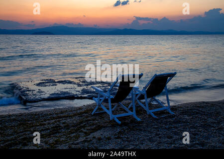 Idyllischer Sonnenaufgang und zwei Liegen am Strand mit Blick auf die Ägäis in Hanioti, Kassandra, Chalkidiki, Griechenland. Stockfoto