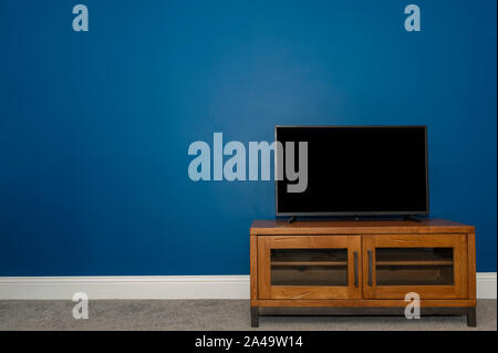 Eine Eiche & Metall TV Gerät und Flachbild-TV gegen einen tiefen Atlantischen blauen Wand Stockfoto