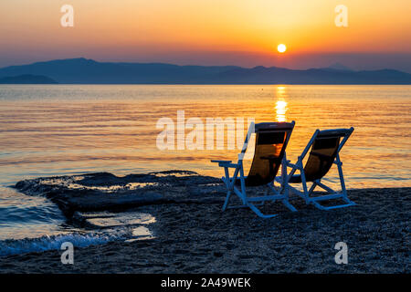 Sonnenaufgang und zwei Liegen am Strand mit Blick auf die Ägäis in Hanioti, Kassandra, Chalkidiki, Griechenland. Stockfoto