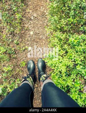 Die Beine der Frauen in wasserdichter Gummistiefel stehen auf einem Waldweg an einem Sommertag. Stockfoto