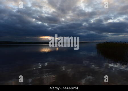 Sonnenlicht aus dunklen Wolken bei Sonnenuntergang spiegelt auf dem See Wasser Stockfoto