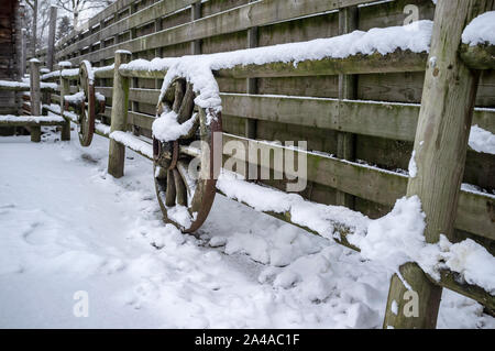 Alten hölzernen Zaun mit Vintage Räder von traditionellen historischen Karren eingerichtet, in einem ländlichen Hof, an einem frostigen Wintertag. Stockfoto