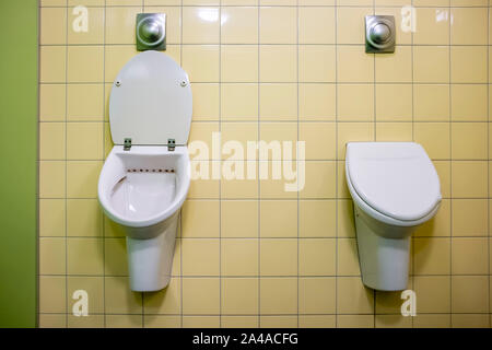 Zwei moderne, weiße Urinale bei den Herren WC, einer offenen, der andere mit einem Deckel verschlossen. Stockfoto