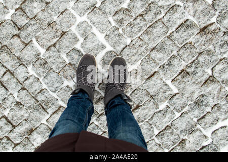 Die Beine der Frauen in der stilvollen Wildleder Stiefel stehen auf der schneebedeckten Fahrbahn aus Granit Pflastersteine, auf einem kalten Winter. Stockfoto