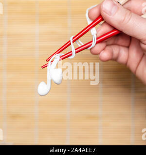 Hand hält ein Kopfhörer mit Essstäbchen auf einem verschwommenen Hintergrund. Konzept der musikalischen Geschmack. Close-up. Stockfoto