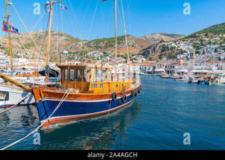 Hydra, Griechenland - 20. Juli 2019; die klassischen Linien des Bootes Kyra Lenia morred um Ufer der Insel mit Bay waterfron Stadt im Hintergrund. Stockfoto