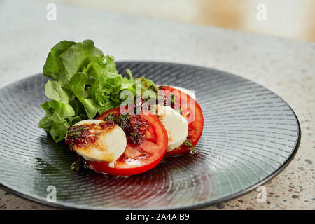 Köstliche Caprese Salat aus Schichten von Tomaten, Mozzarella und grünem Salat, ausgegossen mit Soße, auf schwarzem Teller serviert. Stockfoto