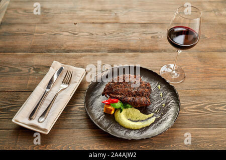 Ansicht von oben Roastbeef Steak auf schwarze Platte mit Käse und Spinat Soße serviert. Gabel, Messer und einem Glas Rotwein auf dem Holztisch. Stockfoto