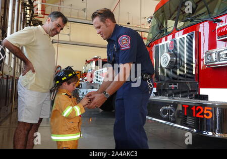 Ein kleiner Junge verkleidet als Feuerwehrmann bekommt sein Idol im Fire Station open house zu erfüllen Stockfoto