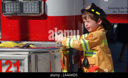 Ein kleiner Junge verkleidet als Feuerwehrmann glücklich ist ein Feuerwehrauto im Fire Station open house zu erkunden. Stockfoto