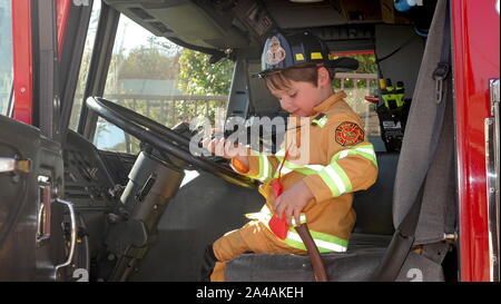 Ein kleiner Junge verkleidet als Feuerwehrmann glücklich ist ein Feuerwehrauto im Fire Station open house zu erkunden. Stockfoto