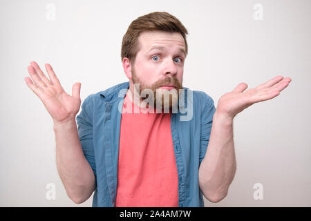 Junge, bärtiger Mann ist überrascht und verwirrt, und hebt seine Hände in Verwirrung. Auf weissem Hintergrund. Close-up. Stockfoto