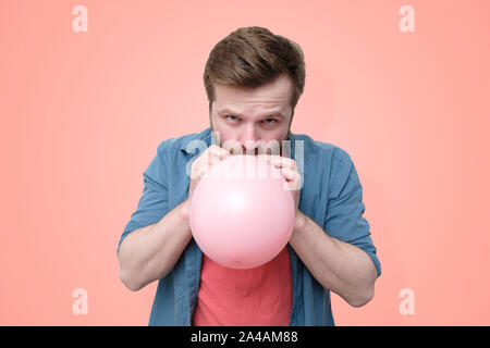 Bärtiger Mann mit einem festen Blick pumpt einen rosa Ball. Isoliert, auf eine Koralle Hintergrund. Close-up. Stockfoto