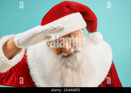 Traditionelle reifen Santa Claus mit grauen Bart tragen rote Kostüm, weiße Handschuhe und Brille gerade suchen Kamera auf blauen Hintergrund. Neues Jahr und Weihnachten Konzept. Stockfoto