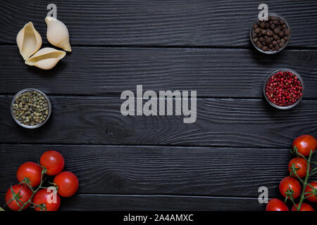 Frische Zutaten für die italienischen Gerichte auf schwarzen Holztisch Hintergrund. Big conchiglie, rote Kirschen, Tomaten und verschiedene Arten von Spice, reg, Stockfoto