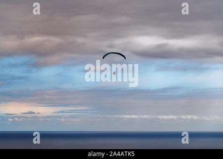 Szene von Gleitschirm über das Meer gegen bewölkt blauer Himmel bei Sonnenuntergang. Portugiesische Insel Madeira Stockfoto