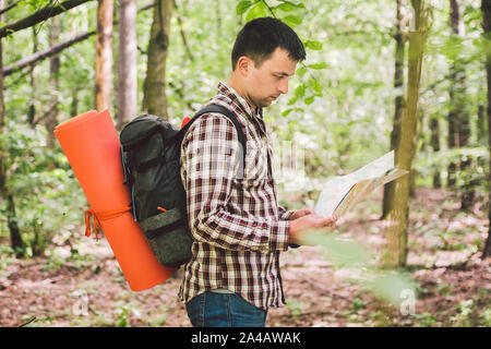 Mann mit Rucksack und Karte Suche Anfahrt in Wilderness Area. Tourist mit Rucksack mit Karte im Wald. Konzept Tourismus Urlaub. Wandern Mann Stockfoto