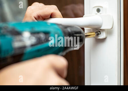 Mann hält in seinen Händen einen elektrischen Schraubendreher und wird die Schraube auf das PVC-Fenster. Close-up. Stockfoto