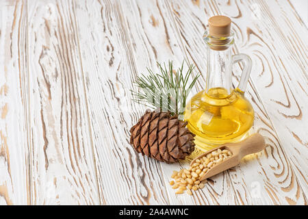 Zeder Öl in Glasflasche mit Haufen von Muttern und Pine Cone auf weissem Holztisch Stockfoto