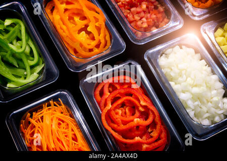 Frische Scheiben von Gemüse in transparenten Kunststoffbehälter auf schwarzem Hintergrund, pflanzlichen Zutaten zum Kochen Stockfoto