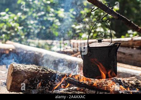 Ein kleiner Wasserkocher mit Wasser ist auf einem Feuer erhitzt, in einem Wald, auf einer sonnigen Tag im Sommer. Close-up. Stockfoto