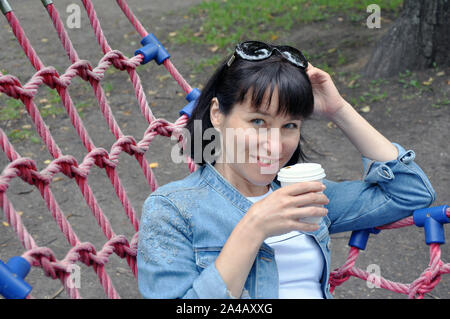 Junge schöne Frau in Pakra auf einem Spaziergang, liegt in einer Hängematte und trinkt Kaffee. Lebensstil Stockfoto