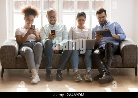 Diverse Jugendliche verwenden elektronische Geräte, sitzen in der Zeile Stockfoto