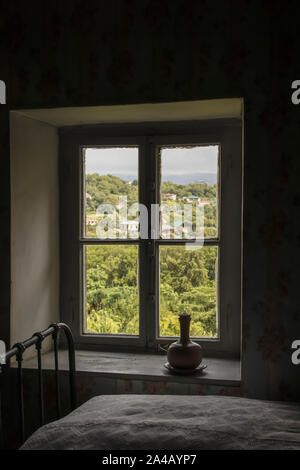 Blick aus Fenster mit alten dicken unvollkommenen Glas alte Landhaus mit schmiedeeisernen Bettgestell und Plüsch Tagesdecke eine Keramik Flasche Wasser zur GEORGISCHEN - Stockfoto