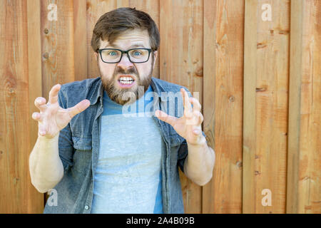 Eine verärgerte bärtiger Mann mit Brille hält seine Hände mit breiten Fingern, als ob Er will jemanden zu schnappen und in die Kamera schaut mit großen Augen, Hav Stockfoto