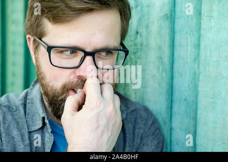 Das Porträt einer gerissen, heimtückischen, Plotten etwas gemeinen Mann, der an der Seite aussieht, entblößt seine Zähne und hält seine Hand in den Mund. O Stockfoto
