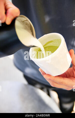 Männliche Barista, vegan Matcha Cappuccino mit hafermilch mit latte Kunst im Café im Freien. Stockfoto