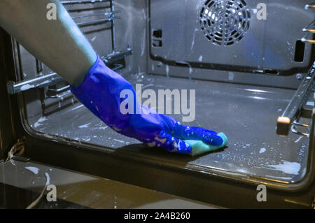 Reinigung der Backofen in der Küche. Hand in einem blauen Haushaltshandschuh. Stockfoto