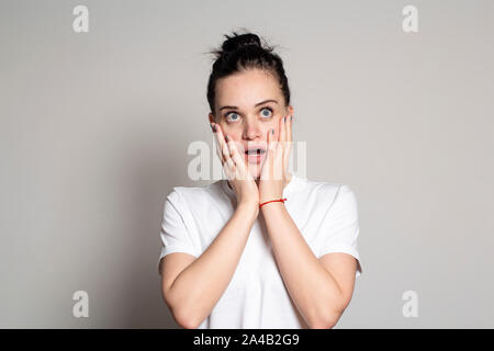 Ein angenehm überrascht, Frau, hält emotional Hände auf ihr Gesicht, öffnet den Mund von angenehm überraschen und schaut sie mit großen Augen an. Am coral Bac isoliert Stockfoto