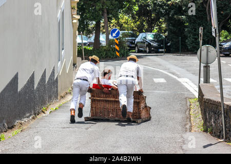 Monte, Madeira, Portugal - 14.September 2019: Rodelpartie mit Carreiros do Monte. Traditionelle Transportmittel, heute eine touristische Attraktion. Menschen reiten bergab mit Treibern. Weidenkorb Schlitten. Stockfoto