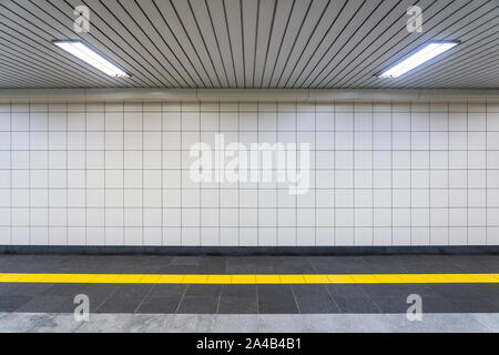 Detailansicht eines regelmäßigen öffentlichen Flur. Niemand ist im Tunnel mit weißen quadratischen Kacheln, Gelb taktiler Pflasterung und weiße Decke. Stockfoto