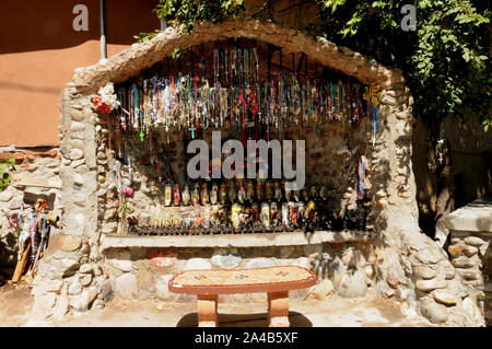 Angebote der Kruzifixe und Kerzen in einer kleinen künstlichen Grotte bei El Santuario De Chimayo, New Mexico. Die Kirche und die Anlage ist ein Bereich der Wallfahrt Stockfoto